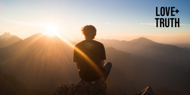 Man looking out to mountains and setting sun, represanting spirituality